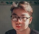 Close-up portrait of a young man wearing eyeglasses in warm light.